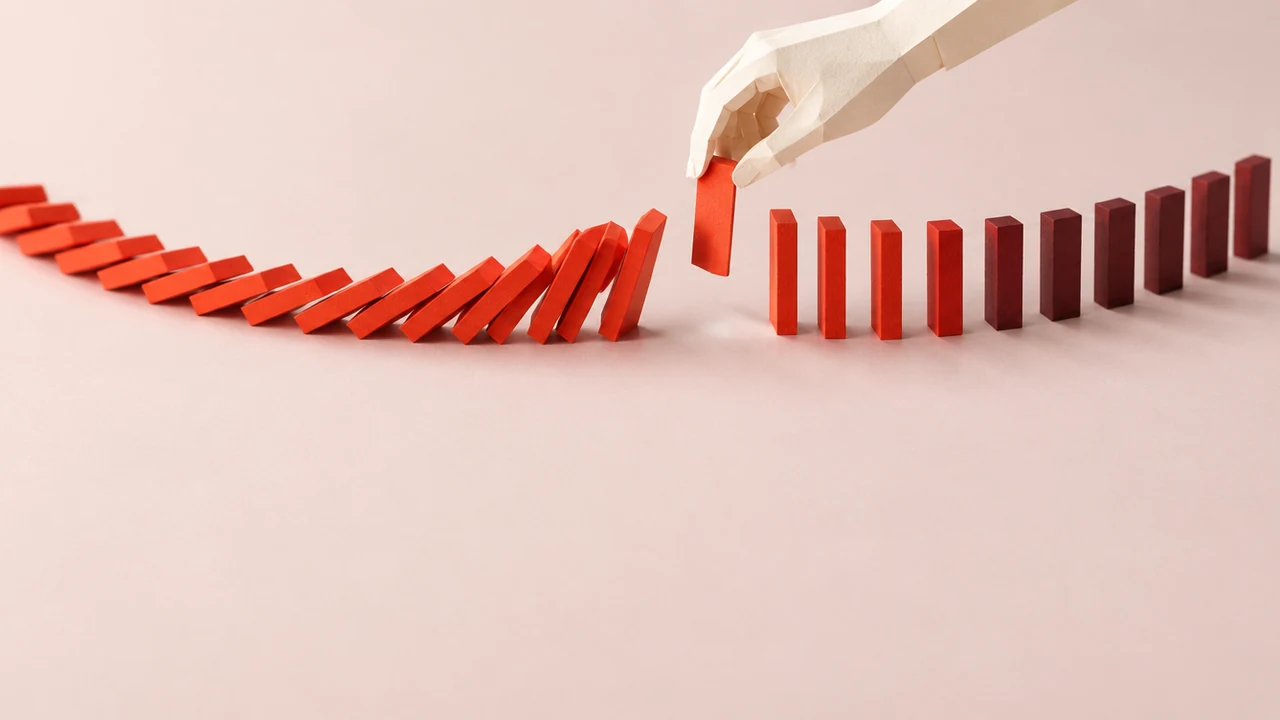 A curving line of red tiles topples from the left while a hand lifts one tile out ahead of the wave, leaving a gap