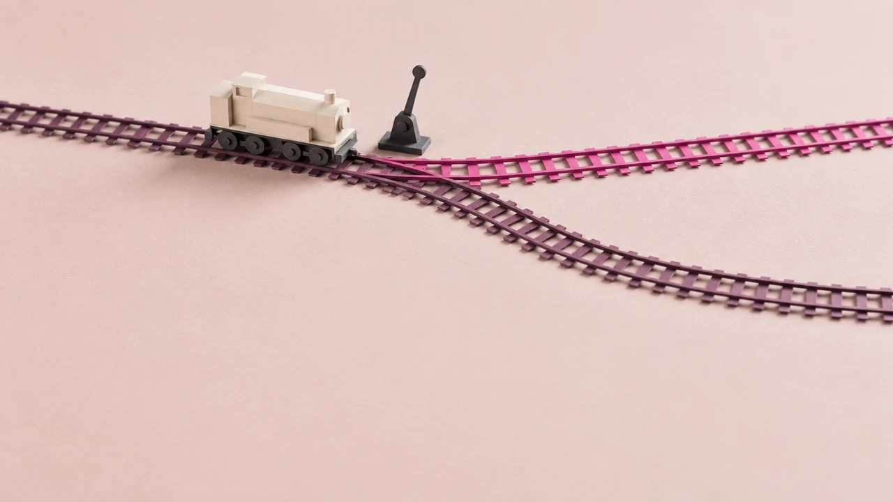 A railway track splits at a set of points beside a tall lever, with a small locomotive waiting before the junction