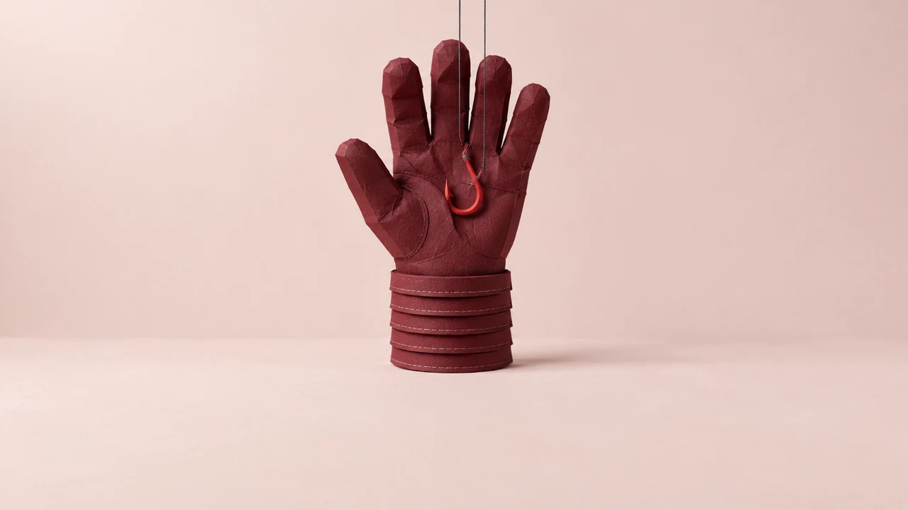 A thick dark red work glove stands upright like a raised hand, its cuff built of stacked layers and a fishing hook snagged harmlessly in its palm