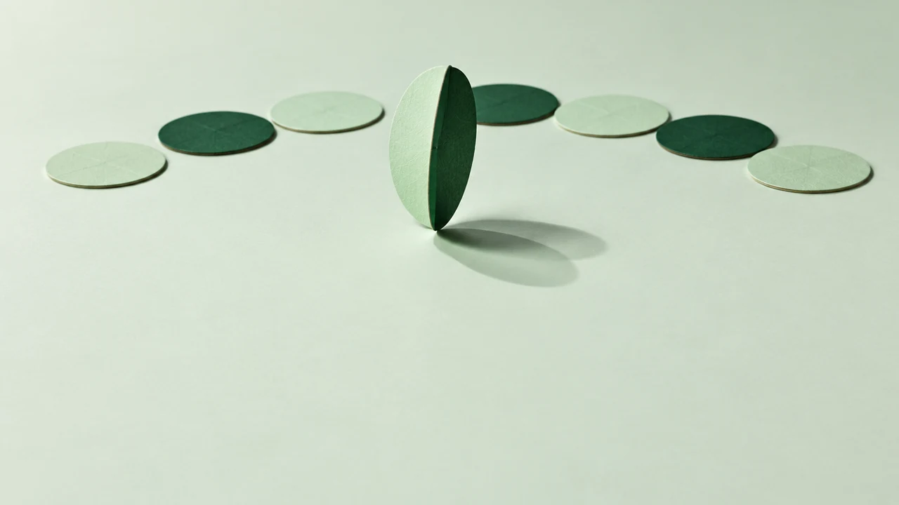 Among flat two-sided paper discs lying jade or dark green side up, one larger disc spins upright on its edge