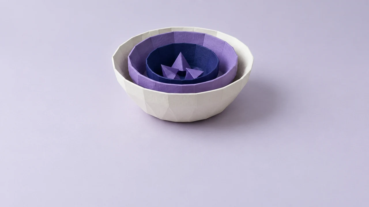 Three nesting paper bowls, warm white, violet and deep indigo, sit one inside another, a few small folded shapes in the smallest