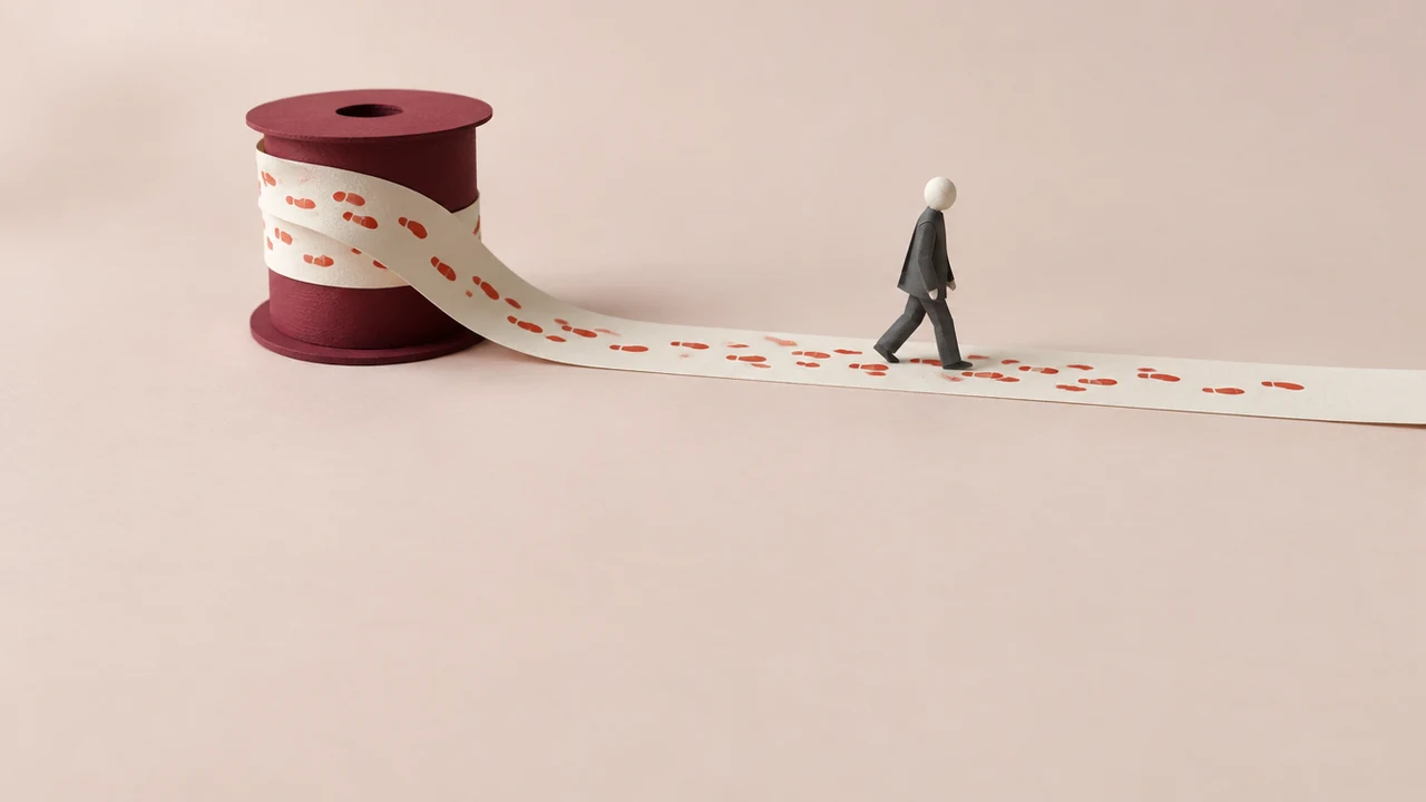 A small paper figure walks along a long runner leaving red footprints, while the printed runner behind winds onto a large spool