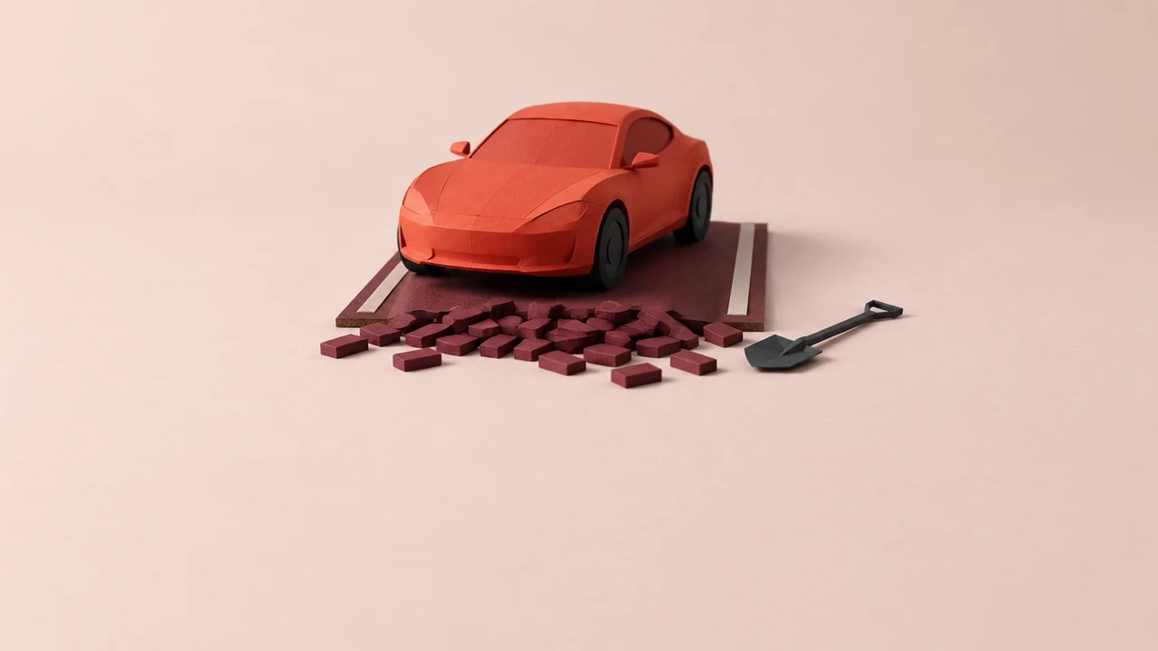 A sleek red sports car sits on a short stretch of road that ends just past its wheels in a heap of unlaid paving blocks